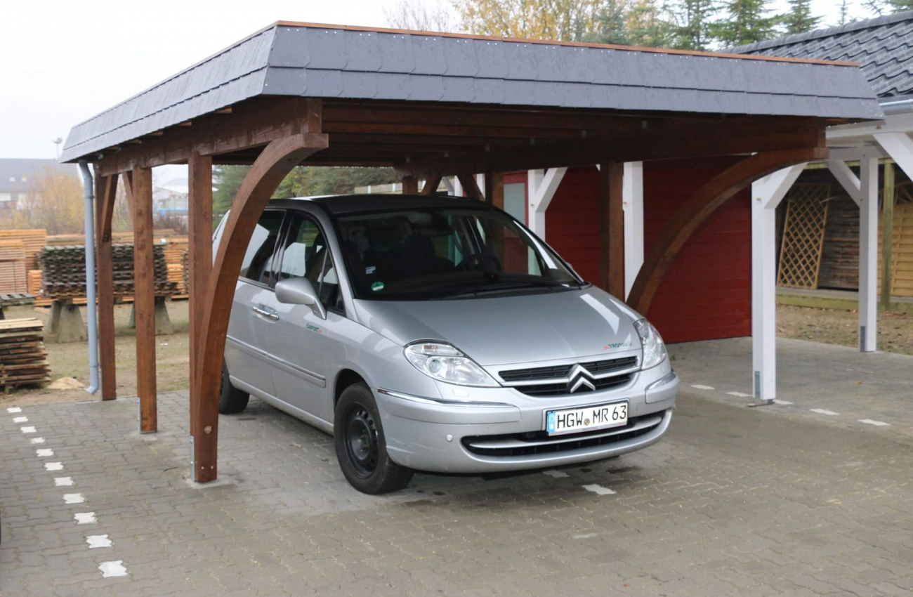 Unter einem Carport aus Holz parkt ein silbernes Auto. Der Carport verfügt über ein flaches Dach. Recht neben dem Carport befindet sich ein weiterer Carport.