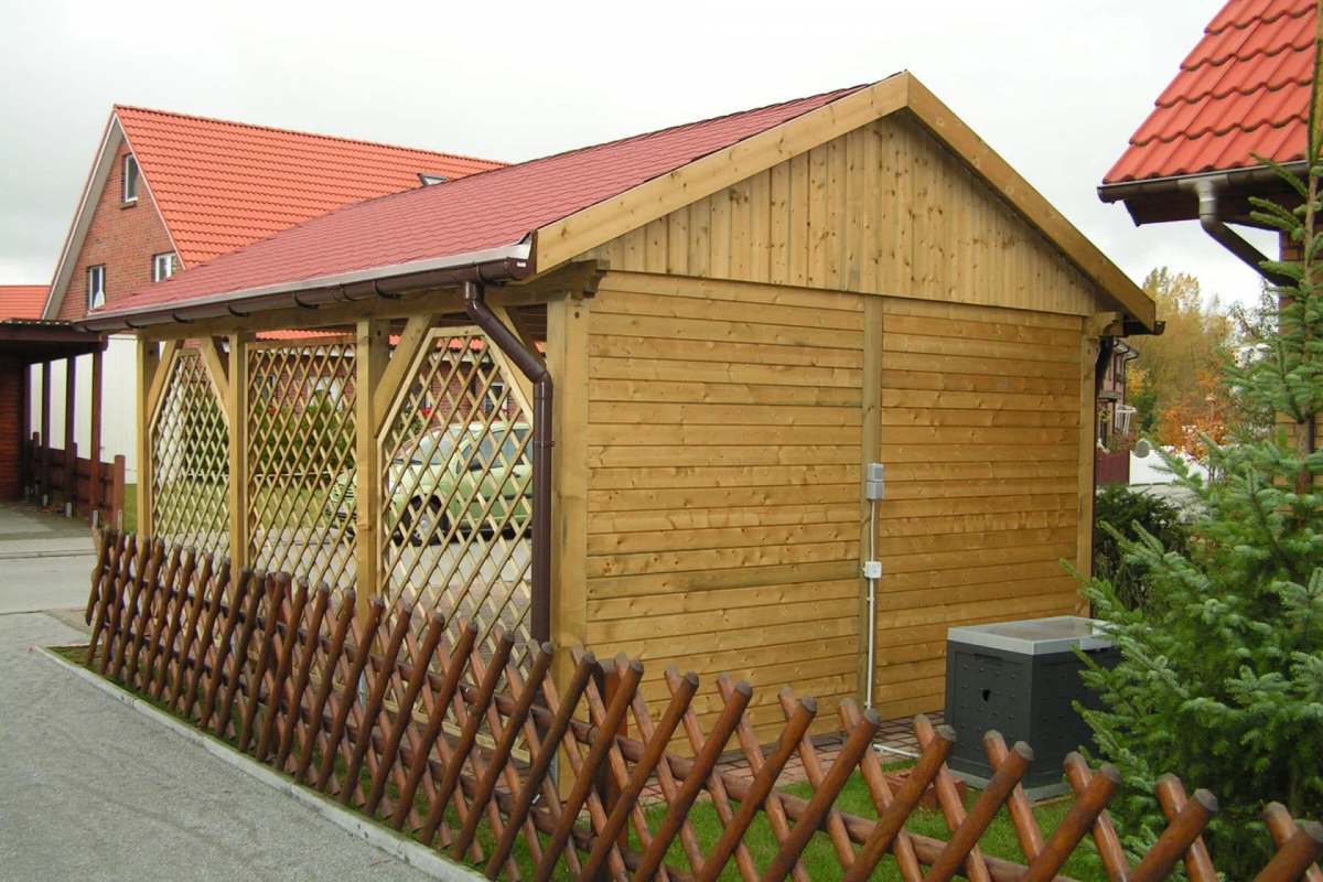 Rückansicht eines modernen Einzelcarports, das aus Holz gefertigt wurde und ein rotes Satteldach besitzt.
