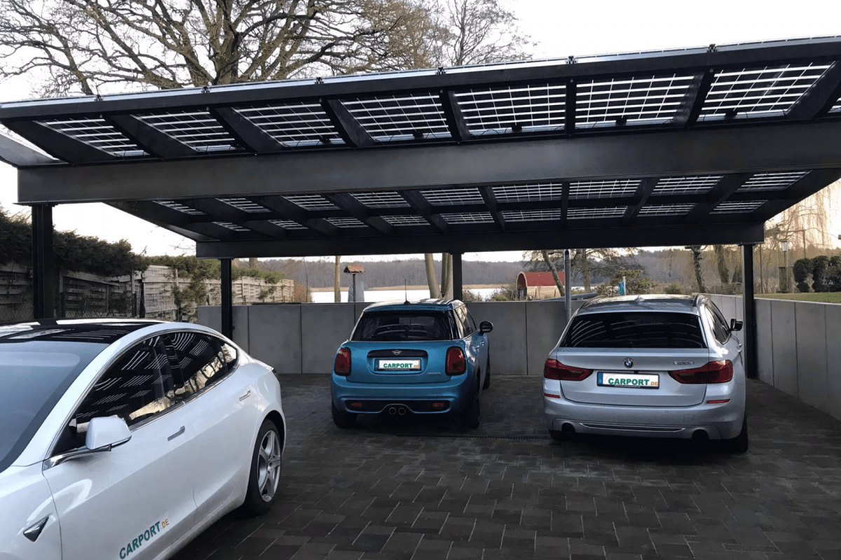 Moderner Solar Carport, der gleich mehrere Parkplätze überdacht. Unter dem Carport parken ein weißes, ein silberfarbenes und ein blaues Auto.