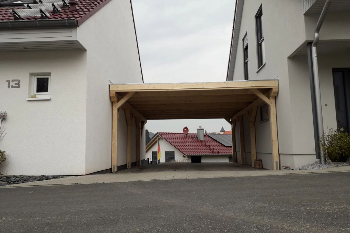 Doppelcarport zwischen zwei Wohnhäusern. Der Carport aus Holz besitzt ein flaches Dach.