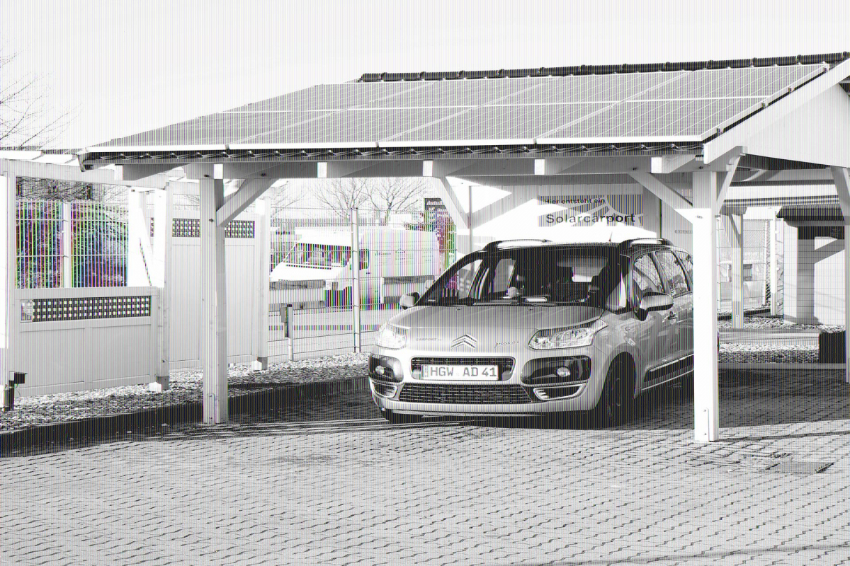 Unter einem weißen Holzcarport parkt ein grünes Auto. Auf dem schwarzen Satteldach des Carports wurden acht Solarpanels montiert.