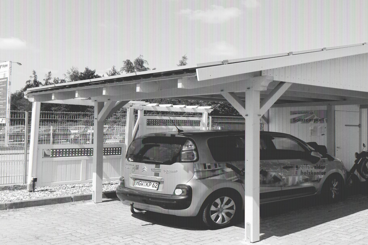 Grüner PKW parkt unter einem Einzelcarport aus Holz. Auf dem Dach des Carports befinden sich einige Solarpanels.